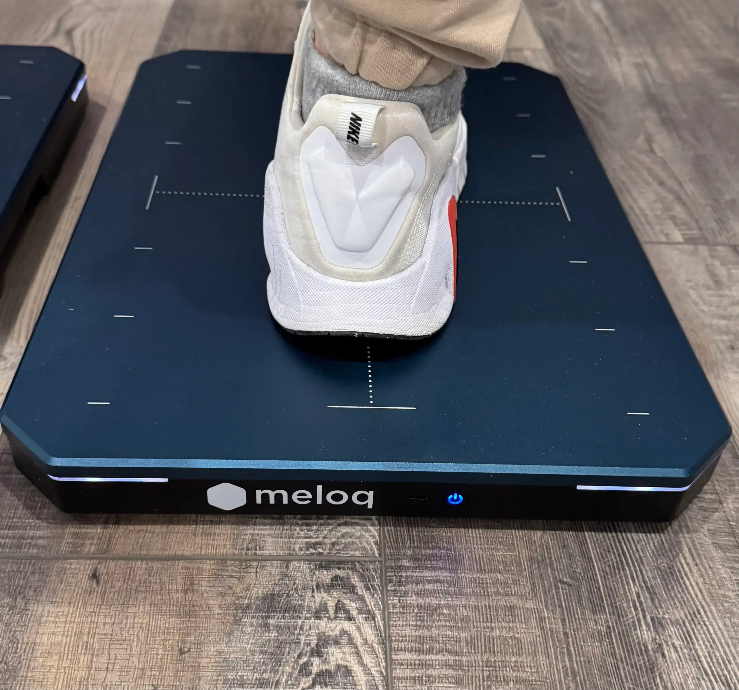 Foot stepping on a black Meloq device on a wooden floor.